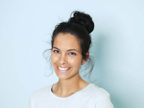 Porträt einer jungen Frau mit schwarzen Haaren, hellblauer Hintergrund, lizenzfreies Stockfoto