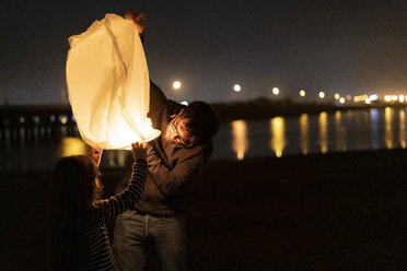 Father and daughter preparing a sky lantern on the beach at night - ERRF01377