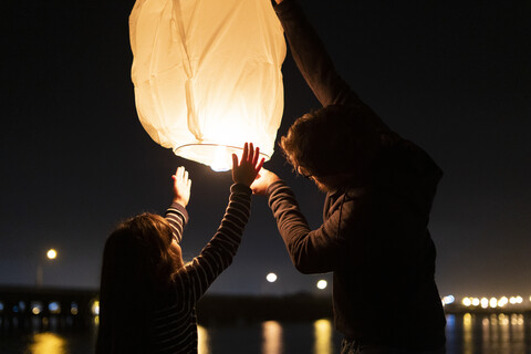 Father and daughter preparing a sky lantern on the beach at night stock photo