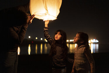 Father and two girls preparing a sky lantern on the beach at night - ERRF01380