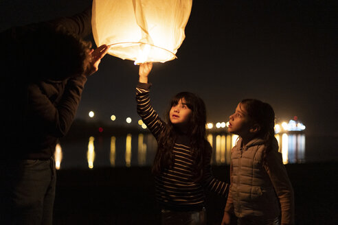 Vater und zwei Mädchen bereiten nachts am Strand eine Himmelslaterne vor - ERRF01380