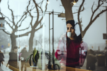 Junge Frau trinkt eine Tasse Kaffee hinter einer Fensterscheibe in einem Café - ACPF00512