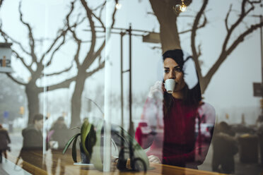 Young woman drinking cup of coffee behind windowpane in a cafe - ACPF00512