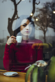 Porträt einer schönen jungen Frau mit einer Tasse Kaffee hinter einer Fensterscheibe in einem Café - ACPF00513