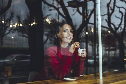 Lächelnde junge Frau mit einer Tasse Kaffee hinter einer Fensterscheibe in einem Cafe - ACPF00514