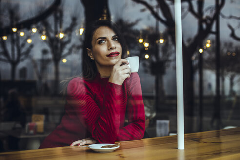 Junge Frau mit einer Tasse Kaffee hinter einer Fensterscheibe in einem Cafe - ACPF00515