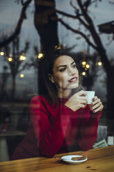 Smiling young woman with cup of coffee behind windowpane in a cafe - ACPF00516