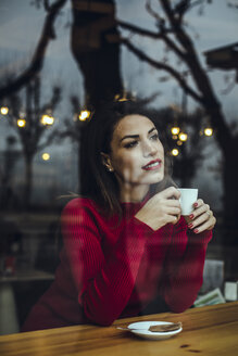 Lächelnde junge Frau mit einer Tasse Kaffee hinter einer Fensterscheibe in einem Cafe - ACPF00516