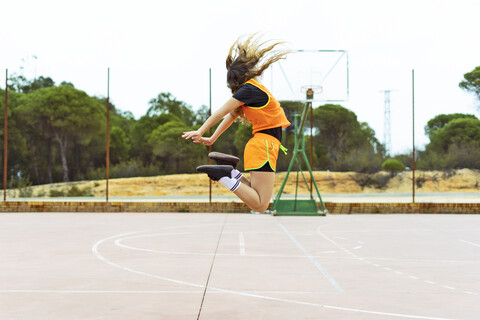 Teenager-Mädchen springt auf Basketballplatz, lizenzfreies Stockfoto