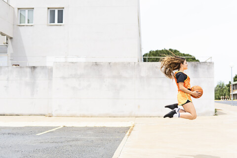 Teenager-Mädchen springt mit Basketball im Freien, lizenzfreies Stockfoto
