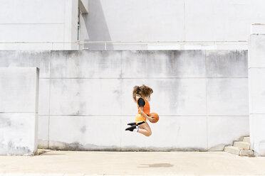 Teenage girl jumping with basketball outdoors - ERRF01391