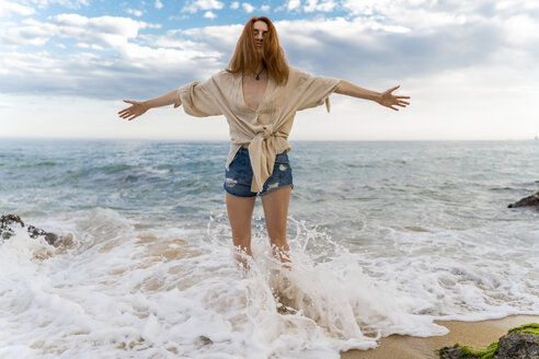 Redheaded young woman standing at seafront with arms outstretched - AFVF02982