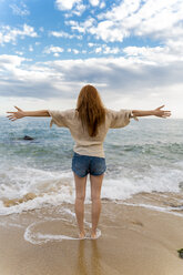 Rückenansicht einer rothaarigen jungen Frau, die mit ausgestreckten Armen an der Strandpromenade steht - AFVF02983