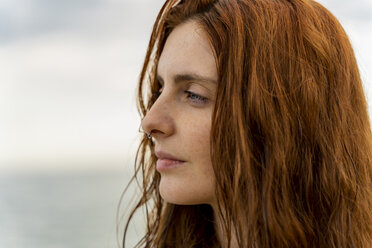 Portrait of pensive redheaded young woman with nose piercing in front of the sea at sunset - AFVF02990