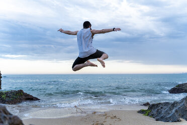 Rückenansicht eines jungen Mannes, der am Strand in die Luft springt - AFVF03007