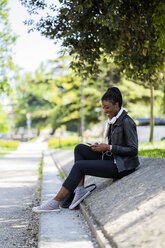 Lächelnde Frau, die sich in einem Stadtpark ausruht und ein Mobiltelefon benutzt - GIOF06349