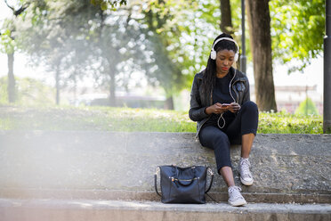 Frau ruht sich in einem Stadtpark mit Handy und Kopfhörern aus - GIOF06350