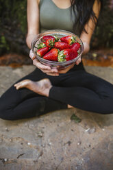 Nahaufnahme einer Frau in Yogastellung, die eine Schale mit Erdbeeren hält - LJF00009