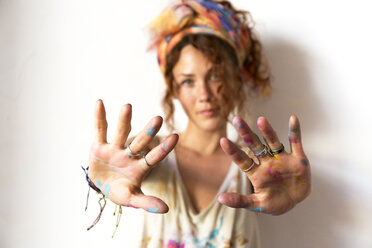 Portrait of young artist in her studio showing her painted hands - JPTF00069