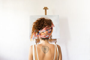 Rear view of young female painter in art studio in front of empty canvas - JPTF00070