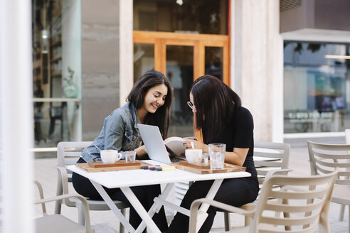 Zwei Freunde sitzen zusammen in einem Straßencafé mit Buch und Laptop - OCAF00383