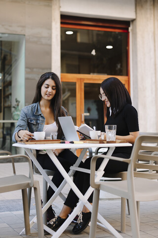 Zwei Freunde sitzen zusammen in einem Straßencafé mit Buch und Laptop, lizenzfreies Stockfoto