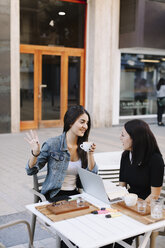 Two friends sitting together at a pavement cafe with laptop - OCAF00390