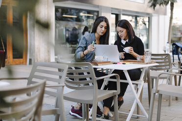 Zwei Freunde sitzen zusammen in einem Straßencafé und benutzen einen Laptop - OCAF00391