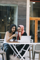 Zwei Freunde sitzen zusammen in einem Straßencafé und telefonieren - OCAF00405