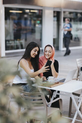 Zwei Freunde sitzen zusammen in einem Straßencafé und telefonieren - OCAF00406