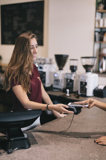 Nahaufnahme einer Frau, die an der Theke eines Cafés bargeldlos mit ihrem Smartphone bezahlt - OCAF00408