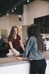 Young woman paying cashless with credit card at the counter of a cafe - OCAF00409