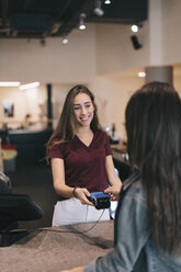 Young woman paying cashless with credit card at the counter of a cafe - OCAF00410