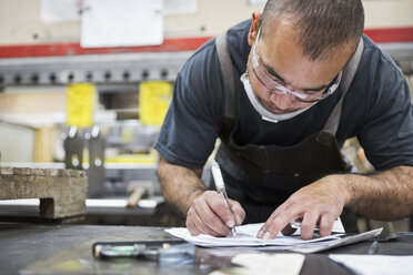 Hispanischer Arbeiter, der in einer Fabrik Papierkram schreibt - BLEF04456