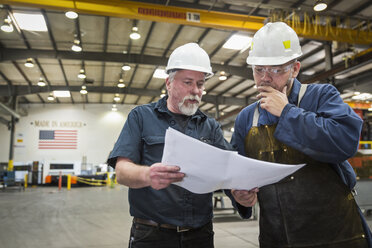 Workers examining paperwork in factory - BLEF04465