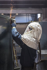 Kaukasischer Arbeiter schleift Metallbehälter in einer Fabrik - BLEF04469