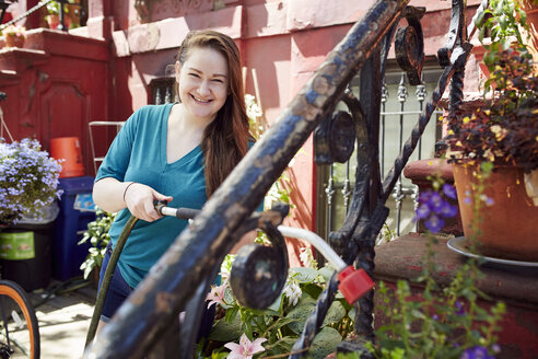 Lächelnde kaukasische Frau, die Pflanzen im Garten gießt - BLEF04518