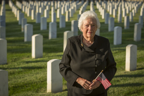Kaukasische Witwe hält amerikanische Flagge auf dem Friedhof, lizenzfreies Stockfoto
