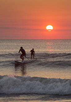 Silhouette von Männern Paddleboarding auf Ozean Wellen - BLEF04529