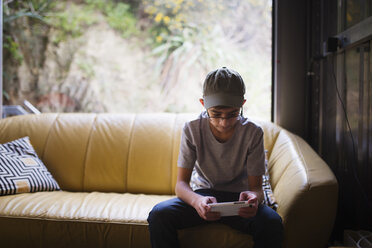 Mixed Race boy sitting on sofa near window texting on cell phone - BLEF04557