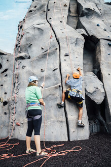 Woman holding rope for man climbing rock climbing wall - BLEF04588