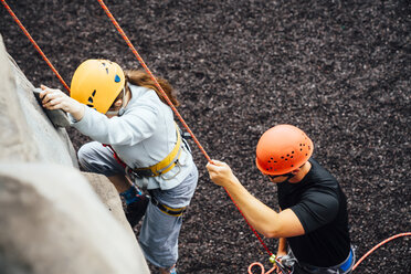 Caucasian man holding rope for woman climbing rock climbing wall - BLEF04591