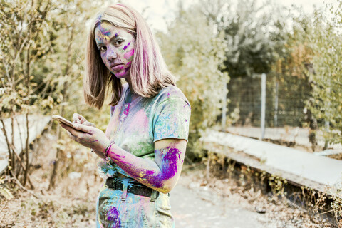 Gir Holi powder colours in her face, using smartphone, Germany stock photo