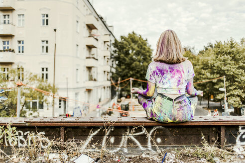 Mädchen mit Holi-Farben auf ihrer Kleidung auf einer Brücke sitzend, Deutschland - VGPF00043