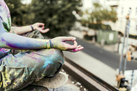 Mädchen mit Holi-Farben auf ihrer Kleidung auf einer Brücke sitzend, Meditation, Deutschland, lizenzfreies Stockfoto