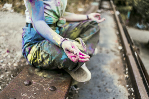 Mädchen mit Holi-Farben auf ihrer Kleidung auf einer Brücke sitzend, Meditation, Deutschland, lizenzfreies Stockfoto