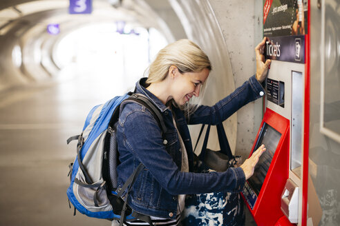 Lächelnde Frau an einem Fahrkartenautomaten im Bahnhof - HMEF00401