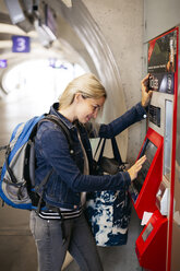 Lächelnde Frau an einem Fahrkartenautomaten im Bahnhof - HMEF00402