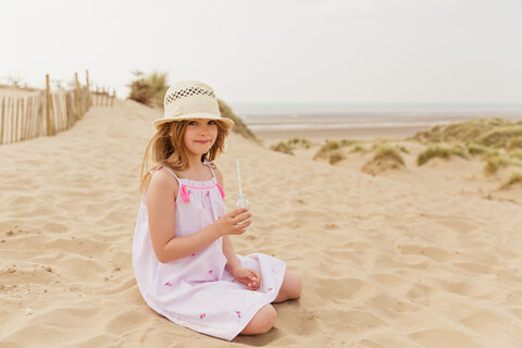 Porträt eines Mädchens, das am Strand sitzt und einen Drink zu sich nimmt, lizenzfreies Stockfoto