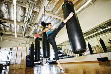 Asian woman kicking heavy bag in gymnasium - BLEF04607